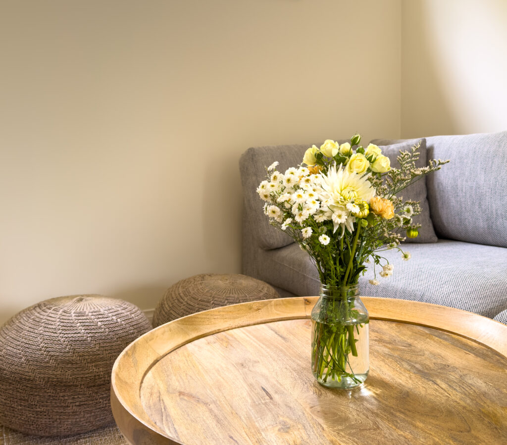 Fresh cut flowers in a jar on a round wooden coffee table in a lounge room